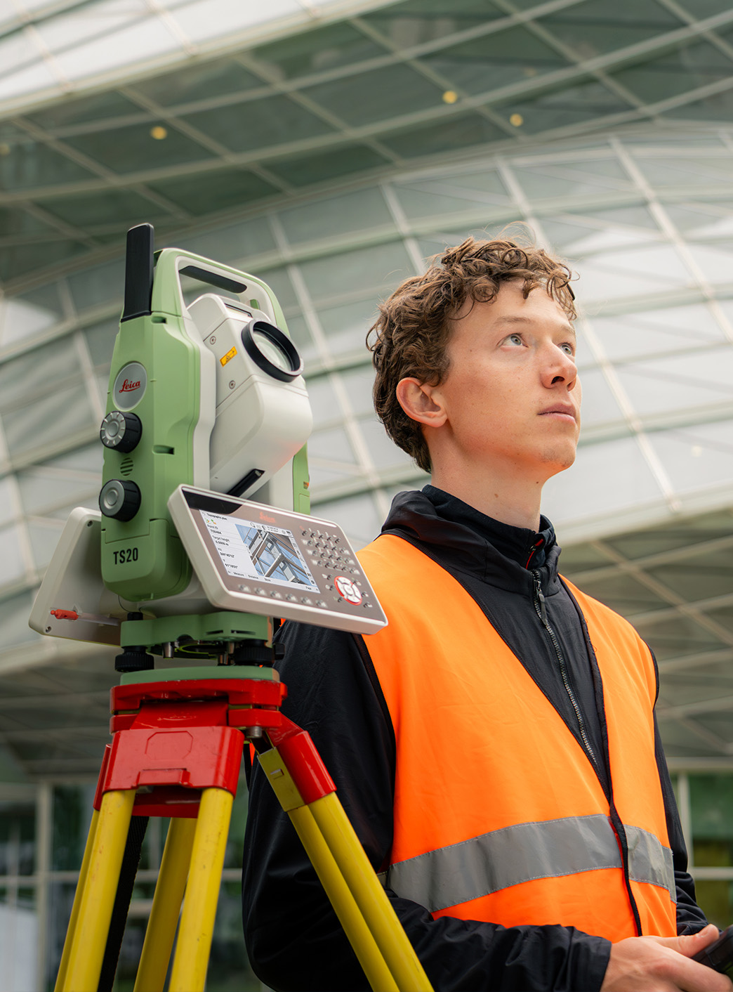 Tecnico in gilet ad alta visibilità accanto a una stazione totale Leica in campo